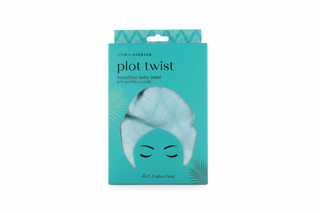 Teal package of 'plot twist' microfiber towel with a face design on a wooden surface